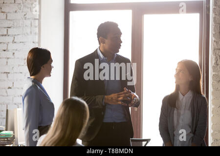 Black boss giving instructions to employees during briefing at office Stock Photo