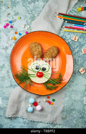 Kids menu, cutlets with mashed potatoes in the form of a hare's head on an orange plate on a gray background Stock Photo