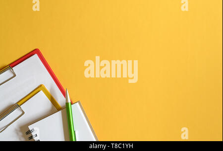 Clipboards, memo pad and green pen on yellow top or desk background. Copy Space Stock Photo