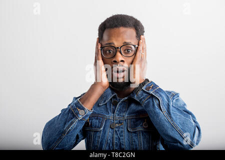 Portrait of surprised dark skinned man in glasses touching his face and opening mouth, being in shok, astonished with some unexpected news isolated on Stock Photo
