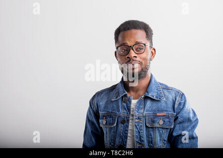 Portrait of good looking confident African American male with small beard wearing casual tshirt and denim jacket posing against gray studio background Stock Photo