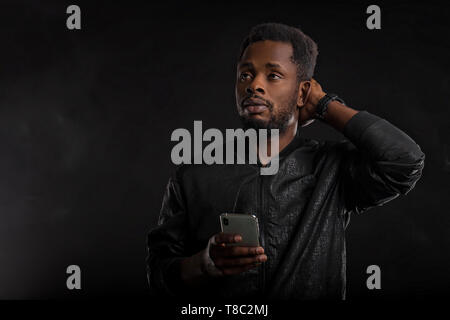 Indoor shot of impressed and amazed attractive African American man with beard and short haircut, holding smartphone, looking surprised at gadget scre Stock Photo