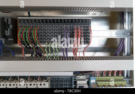 many colorful electrical wires lead into a relay and transformer panel on a wall at an unfinished construction site Stock Photo