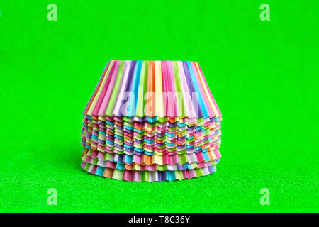 Rainbow colored paper baking cups for muffins and cupcakes on a green background minimal creative concept. Space for copy. Stock Photo