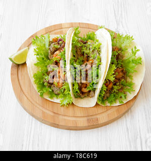 Shrimp tacos on a round bamboo board over white wooden background, side view. Mexican cuisine. Close-up. Stock Photo