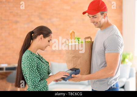 Woman using bank terminal to pay for food delivery indoors Stock Photo