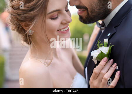 Happy young bride attaching buttonhole to her groom's jacket Stock Photo