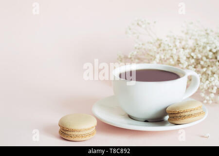 Coffee cup, macaroon and gypsophila flowers on pink background. Stock Photo
