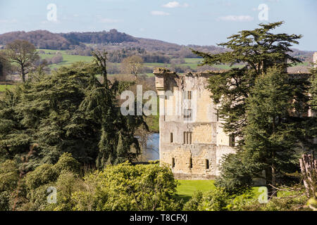 Wardour Castle, near Salibsury in Wiltshire, framed by trees on a bright sunny spring day and surrounded by lush green English countryside hills and f Stock Photo