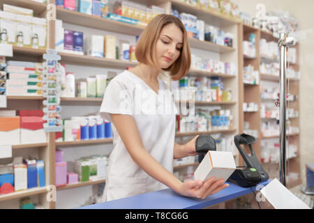 Concentrated woman scanning price of medicament with special barcode scanner. Specialist using device, holding white medical box. Woman working in pharmaceutical industry. Stock Photo
