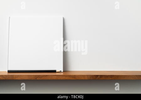 Design concept - front view of square white notebook on bookshelf and white wall for mockup Stock Photo