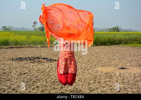 A girl wearing a salwar kameez flying a red dhupatta / clothin the air in a field on a bright day, selective focusing Stock Photo