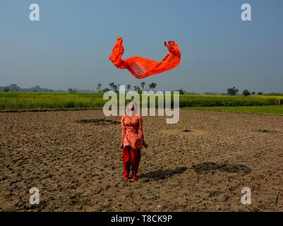 A girl wearing a salwar kameez flying a red dhupatta / clothin the air in a field on a bright day, selective focusing Stock Photo