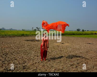 A girl wearing a salwar kameez flying a red dhupatta / clothin the air in a field on a bright day, selective focusing Stock Photo