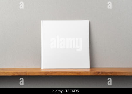 Design concept - front view of square white notebook on bookshelf and grey wall for mockup Stock Photo