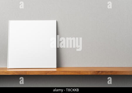 Design concept - front view of square white notebook on bookshelf and grey wall for mockup Stock Photo