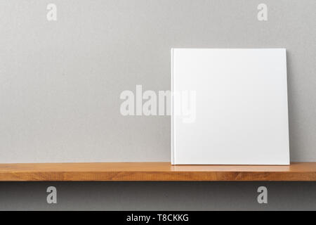 Design concept - front view of square white notebook on bookshelf and grey wall for mockup Stock Photo
