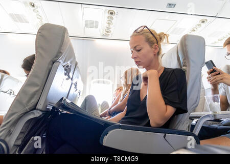 Woman reading magazine on airplane during flight. Female traveler reading seated in passanger cabin. Stock Photo