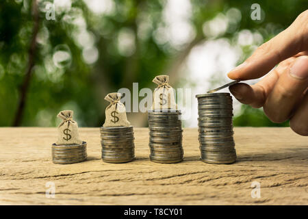 Growing time value of money, investment, wealth financial concept. Hand holding coin, and US dollar bags on rising stacked coins, term sustainable fun