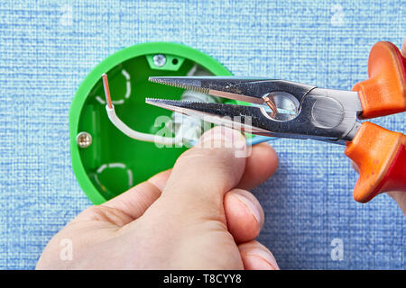 Electric installation work, worker cuts ends of wires of round electrical box with ehlp of pliers. Stock Photo