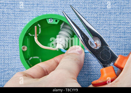 Repairman is installing new round electrical box cutting copper wiring with long nose pliers, electric installation work. Stock Photo