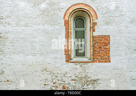 Narrow arched window with bars on the brick plastered wall in old Riga. Stock Photo