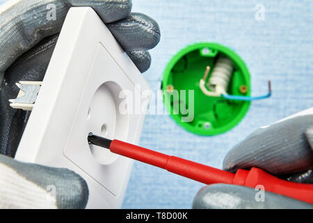 Electrician in protective gloves is twisting screw in new european standard socket with screwdriver with         round outlet box on the background. Stock Photo
