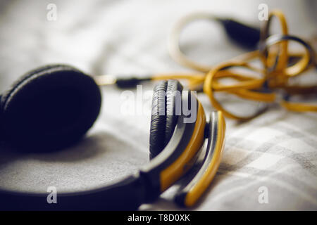 Large yellow headphones with microphone for listening to music and communication lie on the bed on a gray plaid Stock Photo