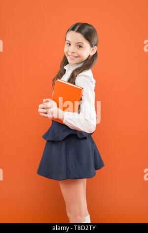 Childhood memories. schoolgirl writing notes on orange background. diary for making notes. get information form book. back to school. Schoolgirl having literature lesson. small girl in school uniform. Stock Photo