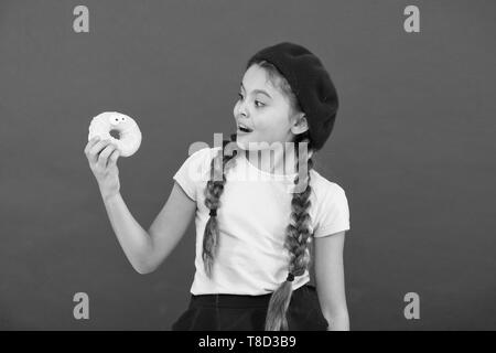 Kids huge fans of baked donuts. Impossible to resist fresh made donut. Girl hold glazed cute donut in hand red background. Kid smiling girl ready to eat donut. Sweets shop and bakery concept. Stock Photo