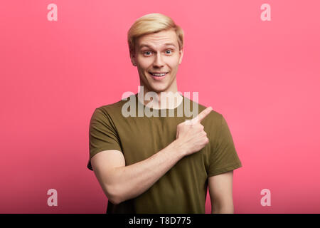 cheerful fair-haired stylish guy pointing the finger at somewhere. isolated pink background. people, gesture concepts Stock Photo