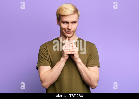 Sly cunning playful man touching chin with finger and looking away, making up a plan, isolated over violet background Stock Photo