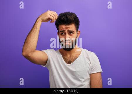 puzzled scared sad nervous depressed man with beard touching his hair, having problems with hair, isolated blue background. depression.bad sampoo. guy's hair turns white, become stumpy and brittle. Stock Photo