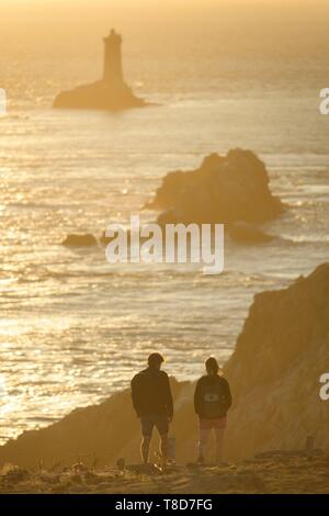 France, Finistere, Plogoff, hiker at sunset at Pointe du Raz, the lighthouse of the Vieille in background Stock Photo