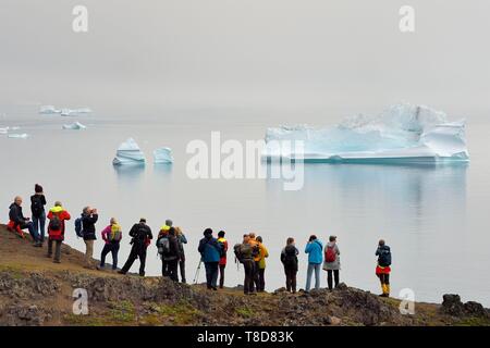 Greenland, west coast, Disko Island, Qeqertarsuaq, hikers on the coast and icebergs in the mist in the background Stock Photo