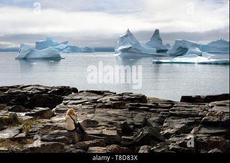 Greenland, west coast, Disko Island, Qeqertarsuaq village bay, hiker on the rocks and icebergs in the background Stock Photo