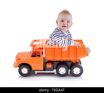 Happy young boy sitting in open-box bed of tipper truck toy, isolated on white background with shadow reflection. Toddler sits on a dumper truck. Ador Stock Photo