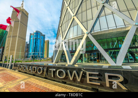 Doha, Qatar - February 17, 2019: base of the iconic Tornado Tower skyscraper in the West Bay area and Flag of Qatar. Tall skyscraper of the Financial Stock Photo