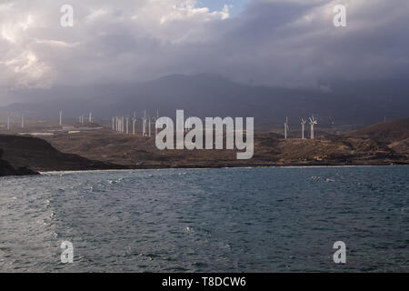 View from the coast on the Atlantic ocean waves. Wind electricity power stations, city and a mountain in the background.Punta de Abona, Tenerife Stock Photo