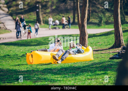 couple laying on yellow inflatable mattress in city park. reading book. drinking smoothies. leisure time Stock Photo
