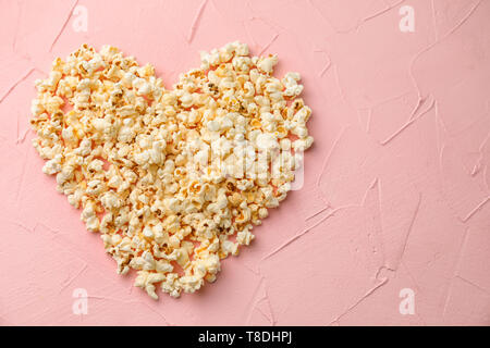 Heart made of delicious popcorn on color background Stock Photo