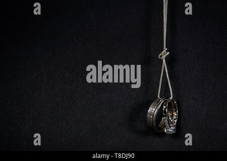 pair of wedding rings hanging from a silver chain with knot isolated on black background Stock Photo
