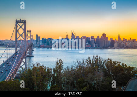 Classic panoramic view of famous Oakland Bay Bridge with the skyline of San Francisco illuminated in beautiful twilight with sunset glow in summer, Ca Stock Photo