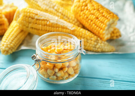 Glass jar with tasty corn kernels and cobs on wooden background, closeup Stock Photo