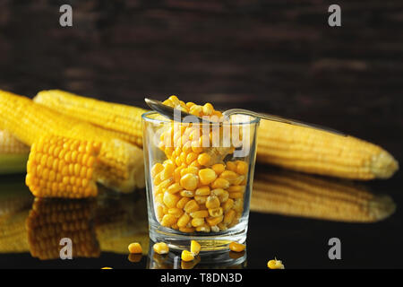 Glass with tasty corn kernels on table against dark background Stock Photo
