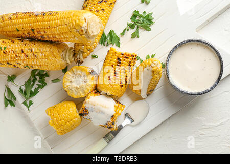 Tasty grilled corn cobs with sauce on white board Stock Photo