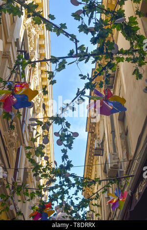 Colorful windmills and flowers decorations against the blue sky on a narrow street with old buildings in Bucharest, Romania Stock Photo