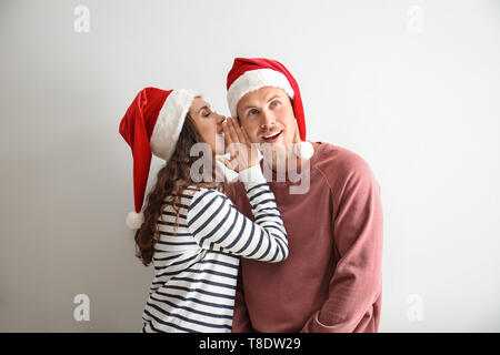 Portrait of cute young woman in Santa hat telling secret to her boyfriend on white background Stock Photo