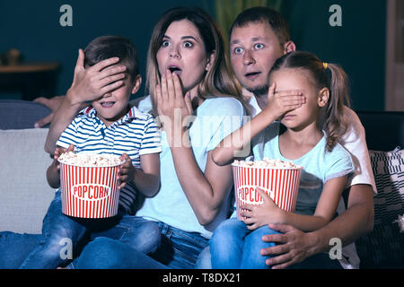 Family eating popcorn while watching scary movie in evening Stock Photo