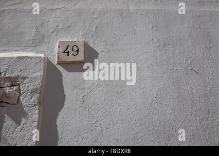 White house street number forty-nine 49 carved into marble parallelepiped full with black paint, white-washed buildings in Noci, Puglia, Italy with summer day shadows Stock Photo